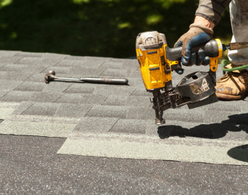 Professional Plymouth roofer using a nail gun to repair shingles on a roof