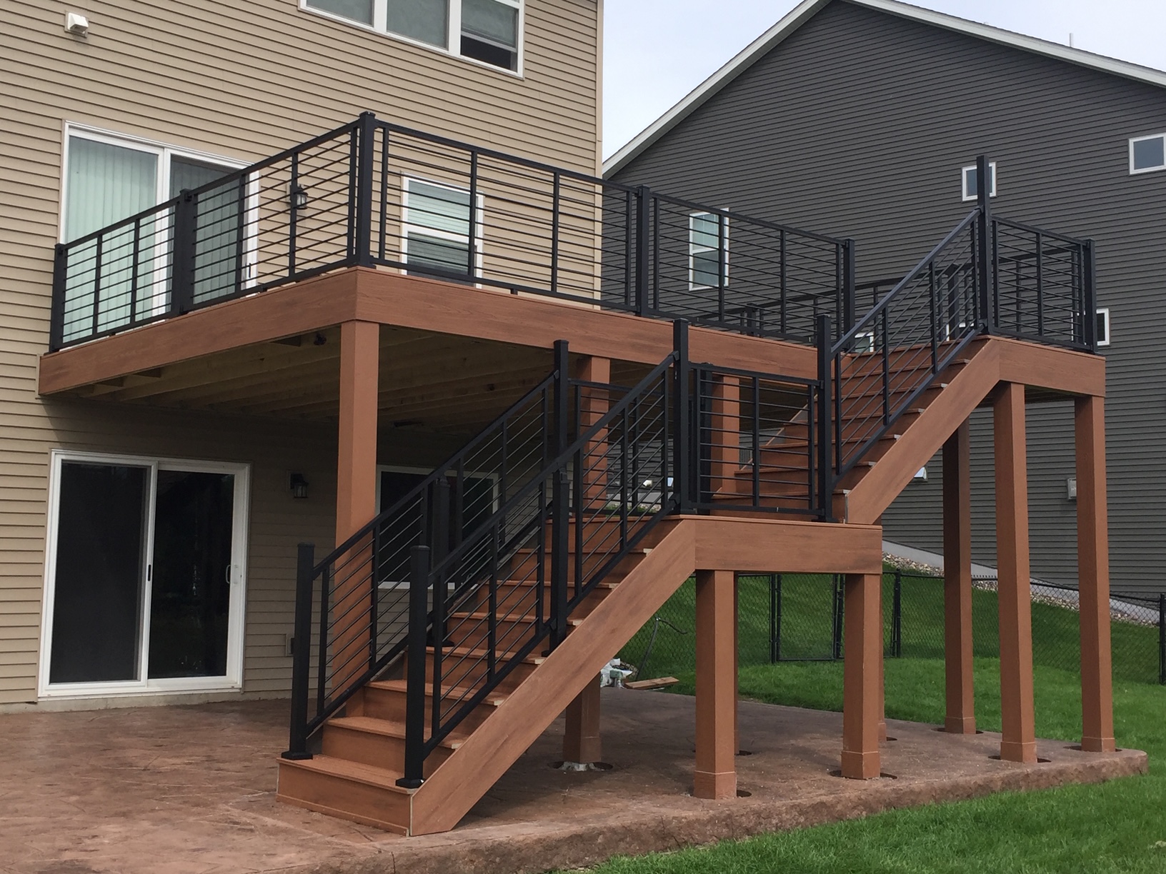 Raised wood-tone deck with black cable-style railings and two stair runs