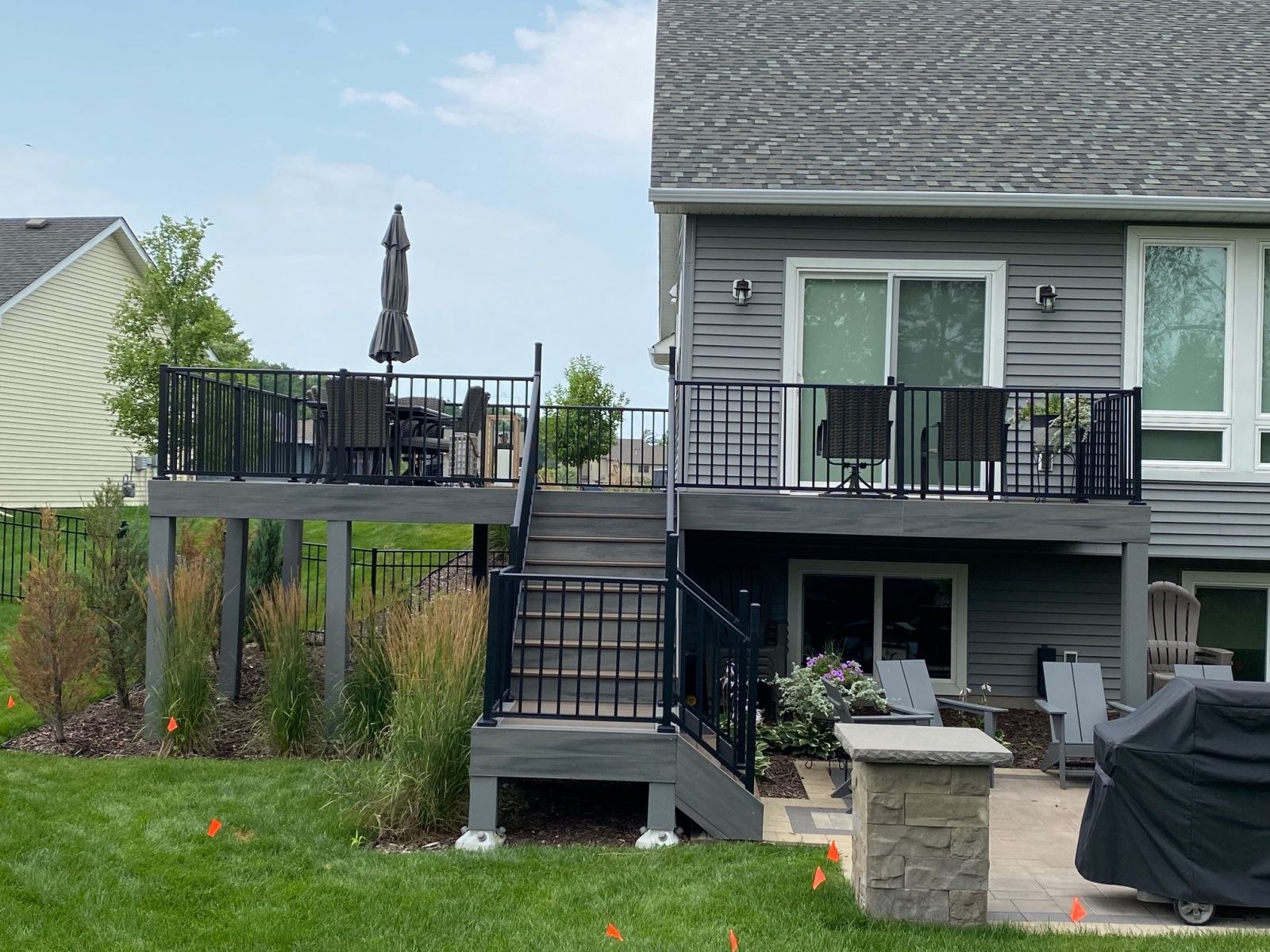 Elevated gray deck with black railings, a central staircase and patio seating below