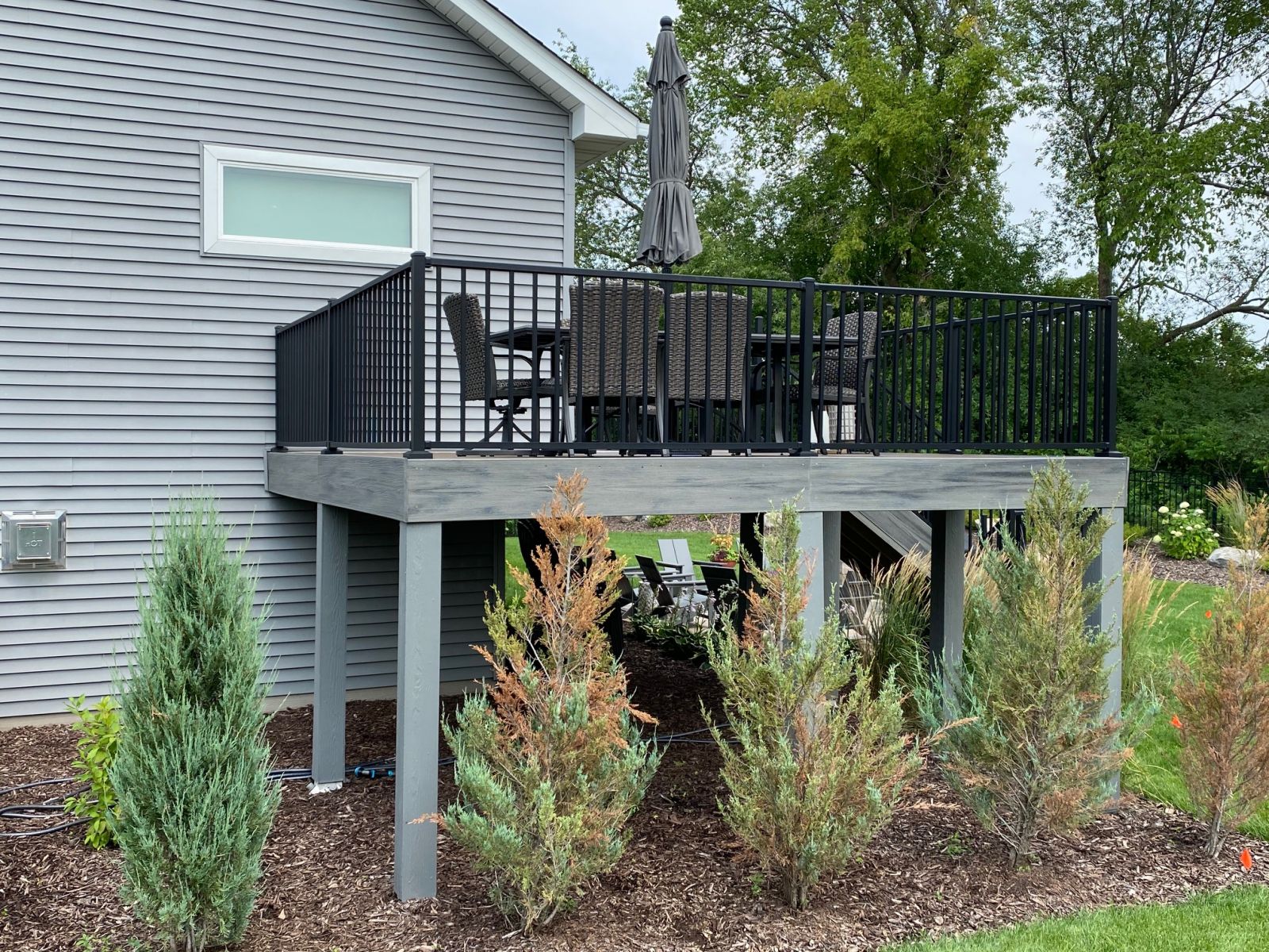 Finished gray deck with black metal railing beside a gray-sided home