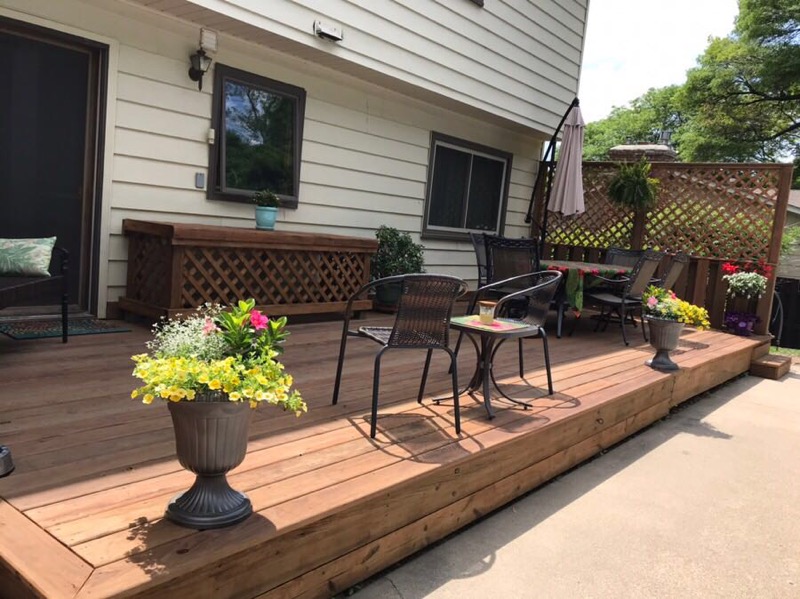 Ground-level wood deck with outdoor chairs and flower planters beside a home