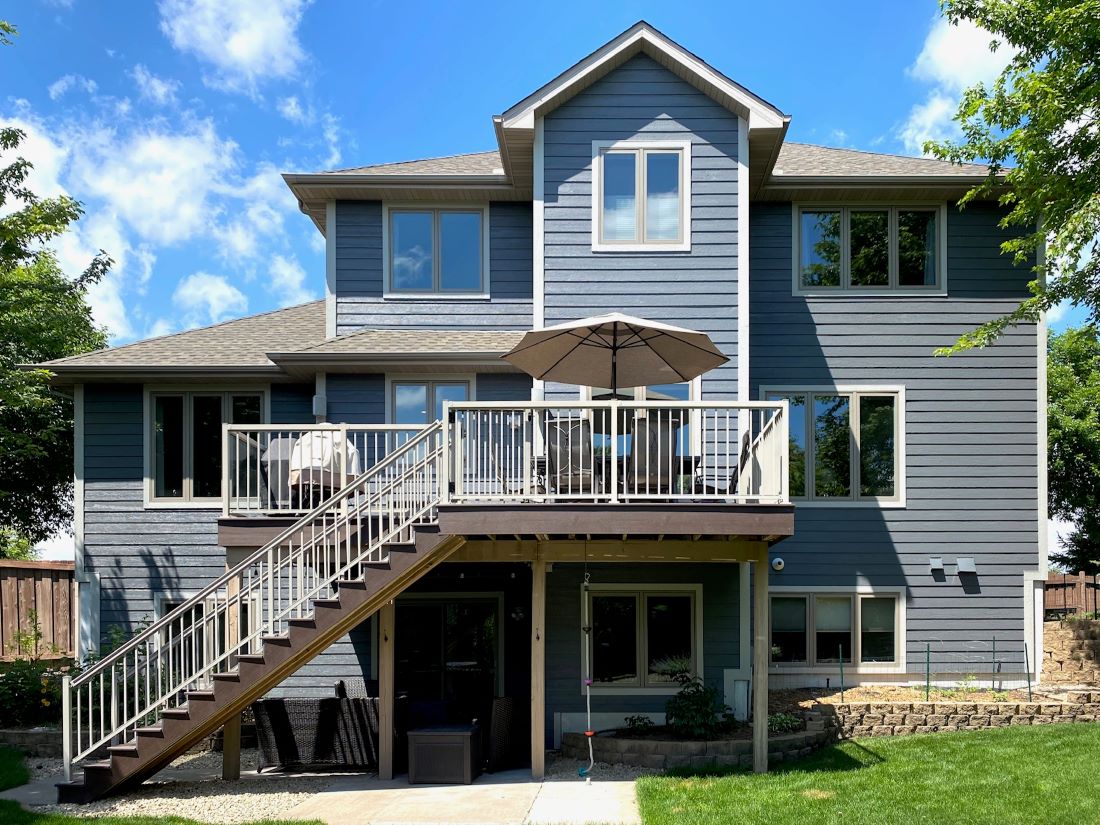 Completed gray lap siding on the rear of a two-story home with a raised deck